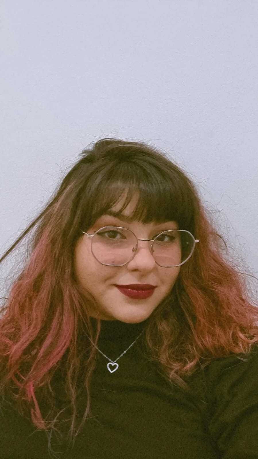 Retrato de Rafaelly Rodrigues: cabelo castanho com pontas rosadas, óculos de armação fina e sorriso discreto